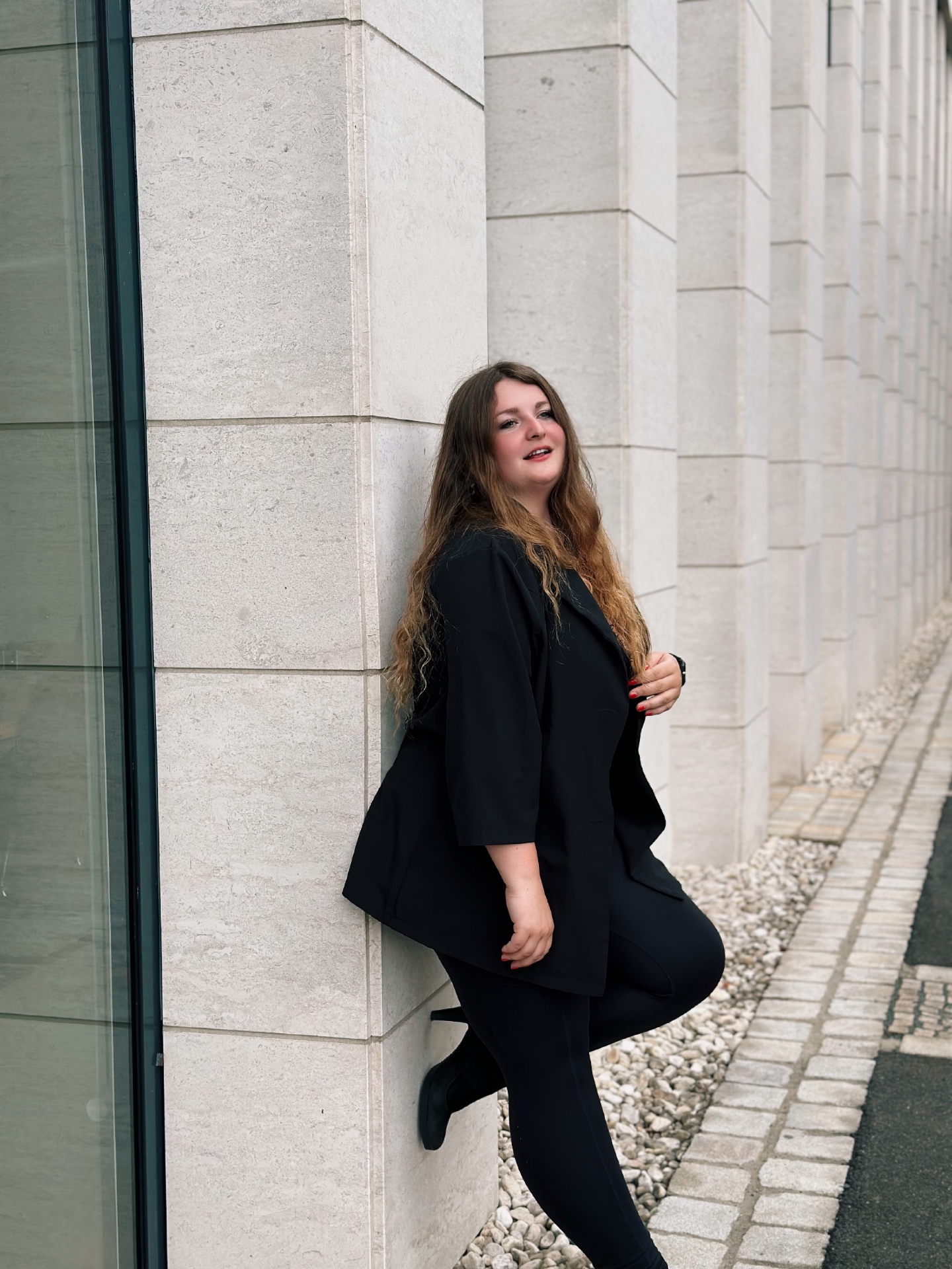 Stella Pollak in schwarzem Blazer an einer modernen Steinfassade
